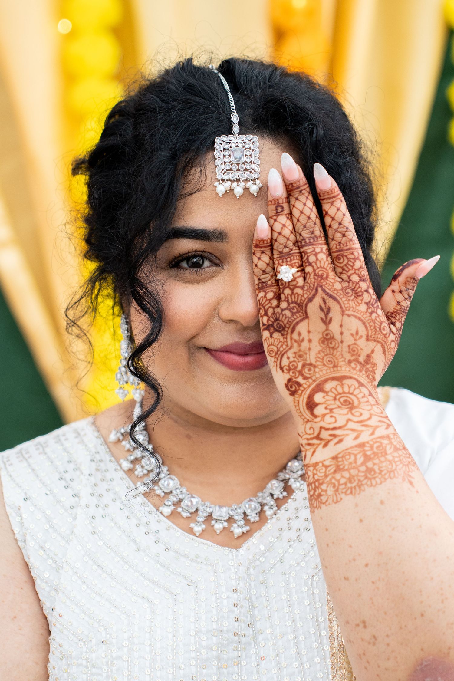 Indian bride in white lehenga showcasing intricate mehndi henna designs on her hand.