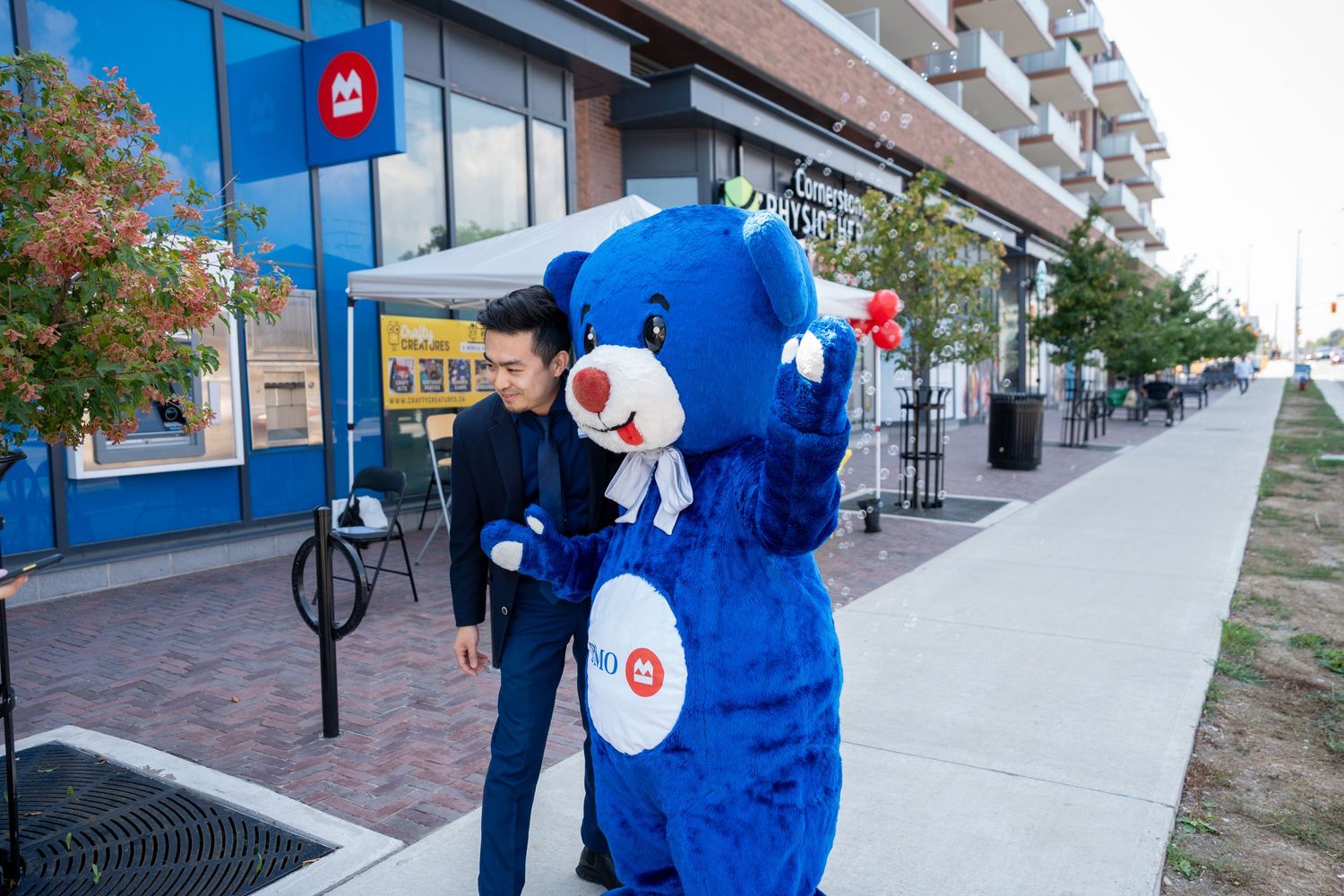 Man interacting with BMO blue bear mascot outside a BMO bank location.