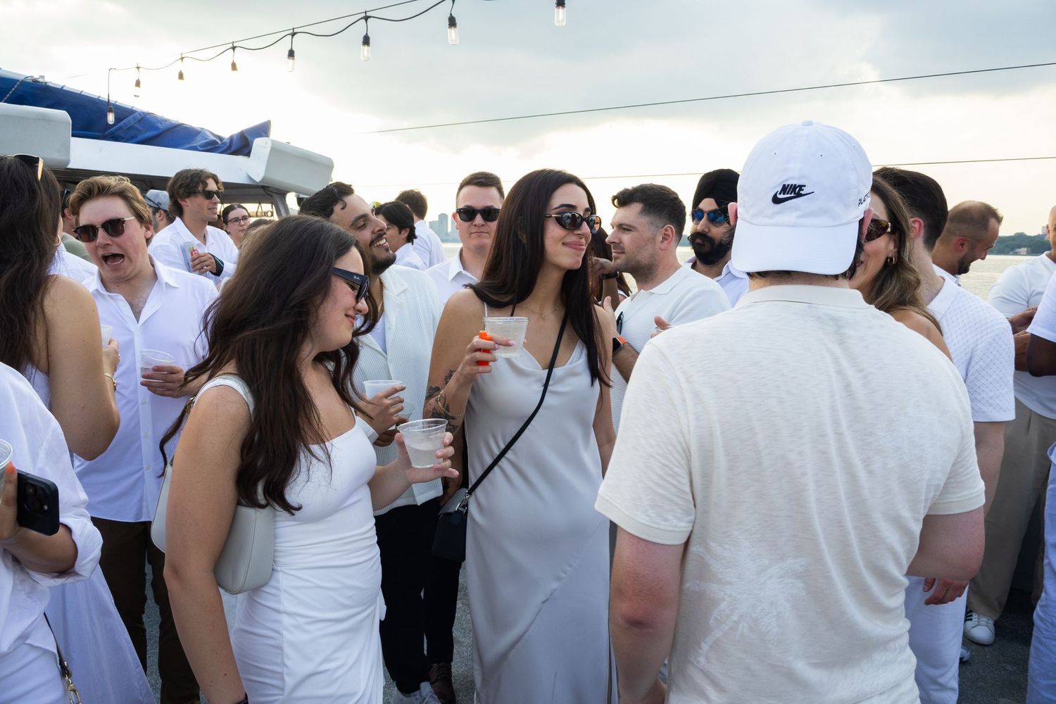 Crowd of guests dressed in white mingling at an outdoor rooftop party.