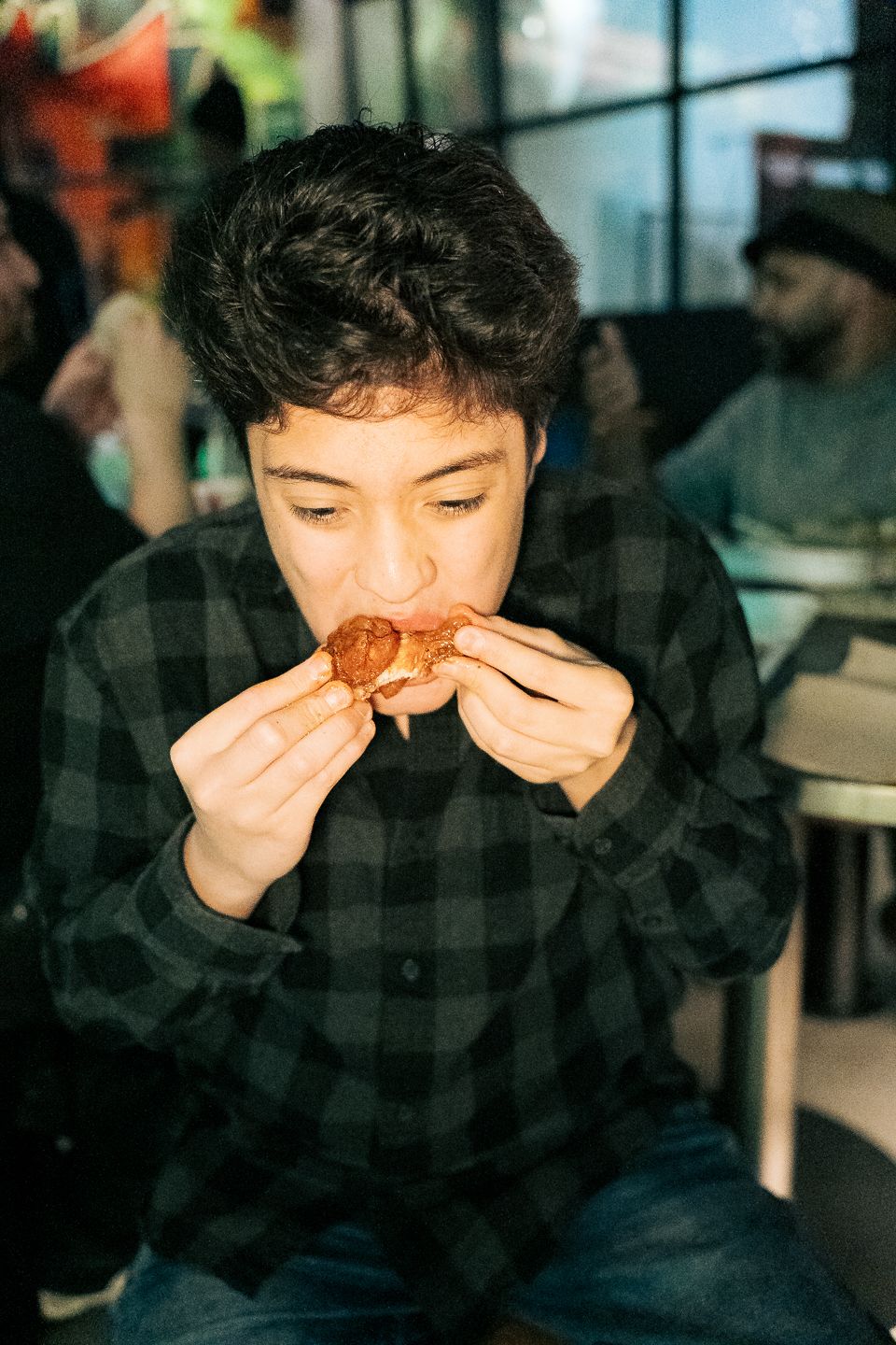 Young man in plaid shirt eating a chicken wing at a Wings restaurant.