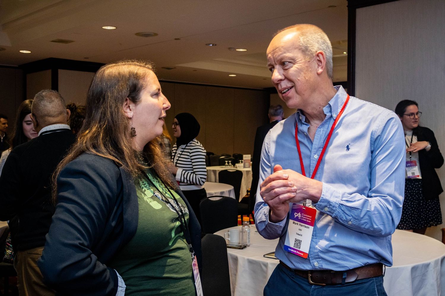 Man and woman engaged in conversation at professional conference networking reception with tables behind them.