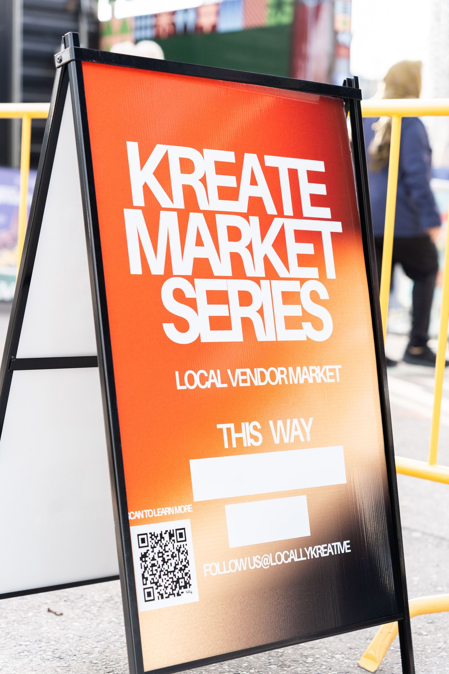 Orange Kreate Market Series local vendor market directional sign with QR code on city sidewalk.