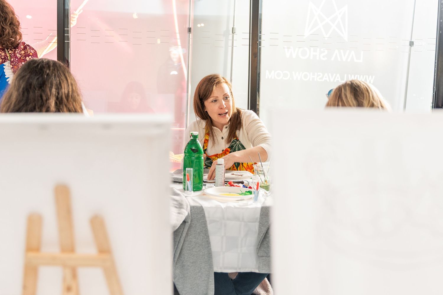 Woman painting at an art workshop table with green water bottle and art supplies at a creative market event.