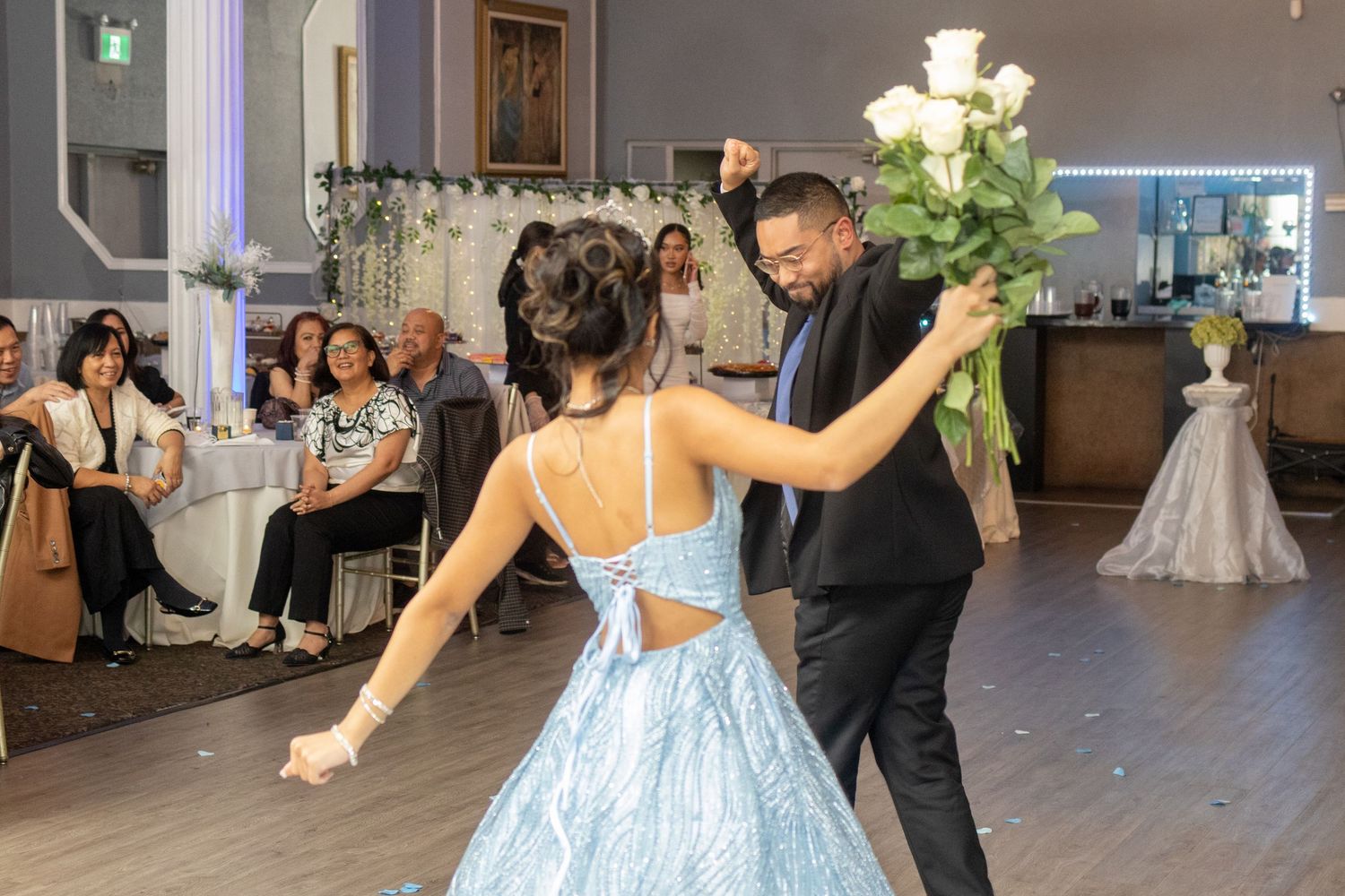 Young woman in light blue gown dancing with partner holding white roses at her 18th birthday debut.