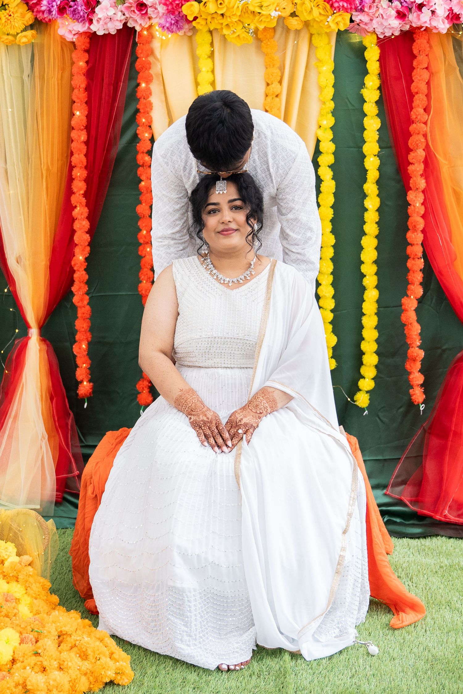 Bride in white lehenga receiving a kiss on head at a traditional Indian wedding ceremony.
