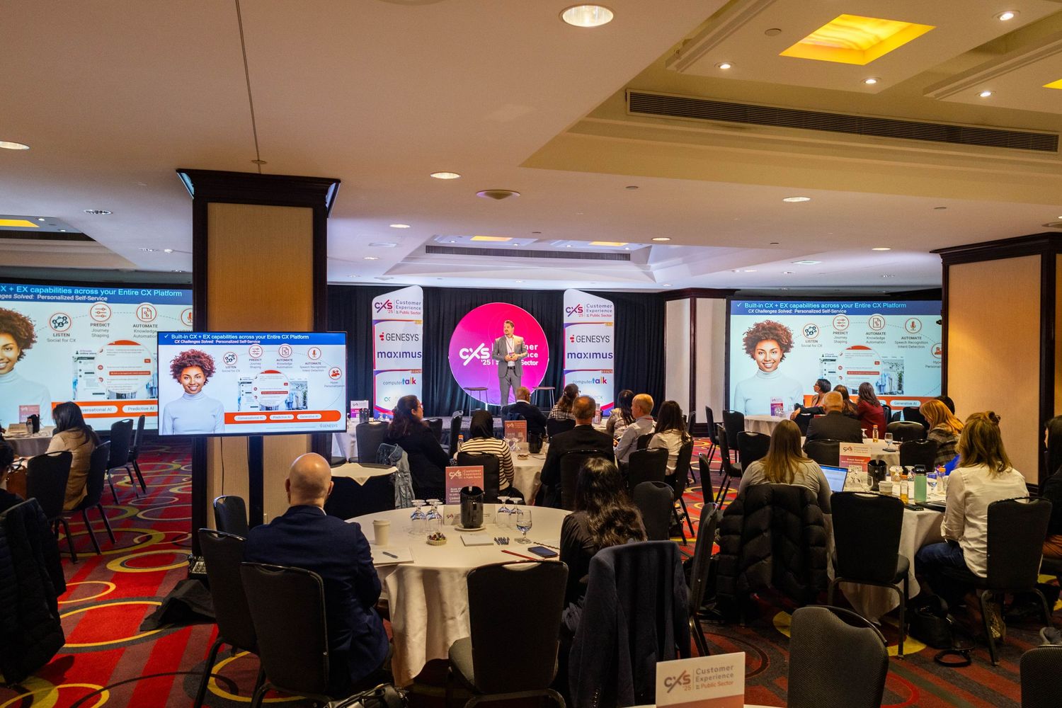 Large conference ballroom with round tables and attendees watching a presentation on big screens.