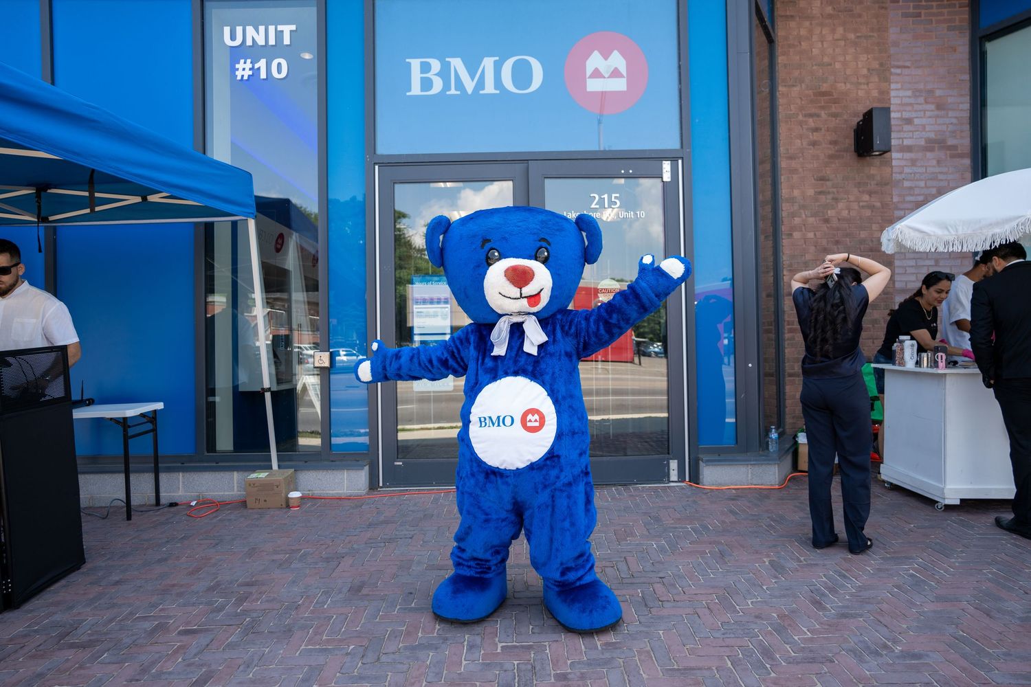 BMO blue bear mascot posing alone outside Unit 10 BMO bank branch.