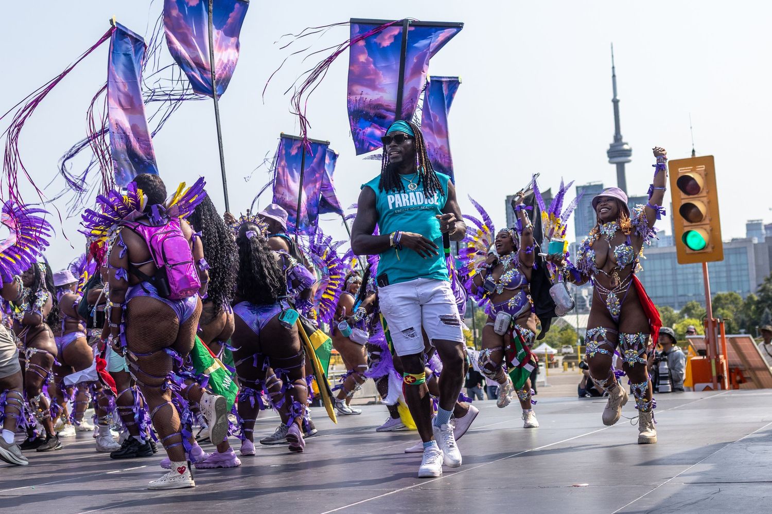Carnival dancers in purple costumes parading down a city street with the CN Tower in background.