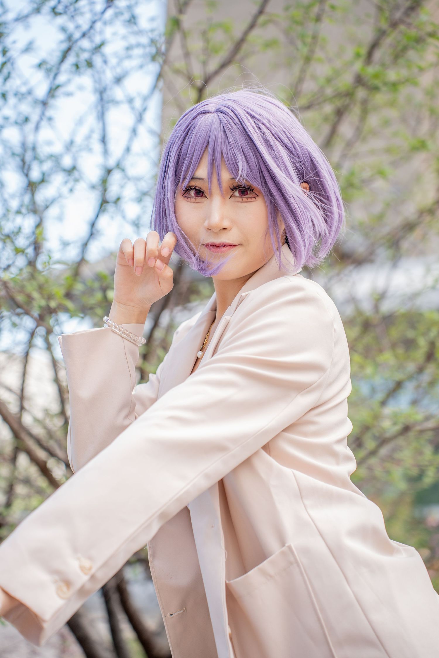 Cosplayer with purple bob wig in white blazer posing outdoors among spring trees in anime-inspired costume.