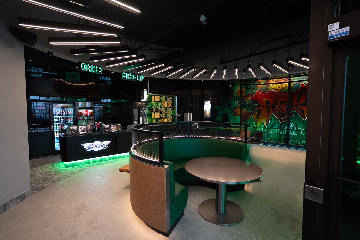 Modern fast casual restaurant interior with green booth seating, neon lighting, and graffiti wall art.