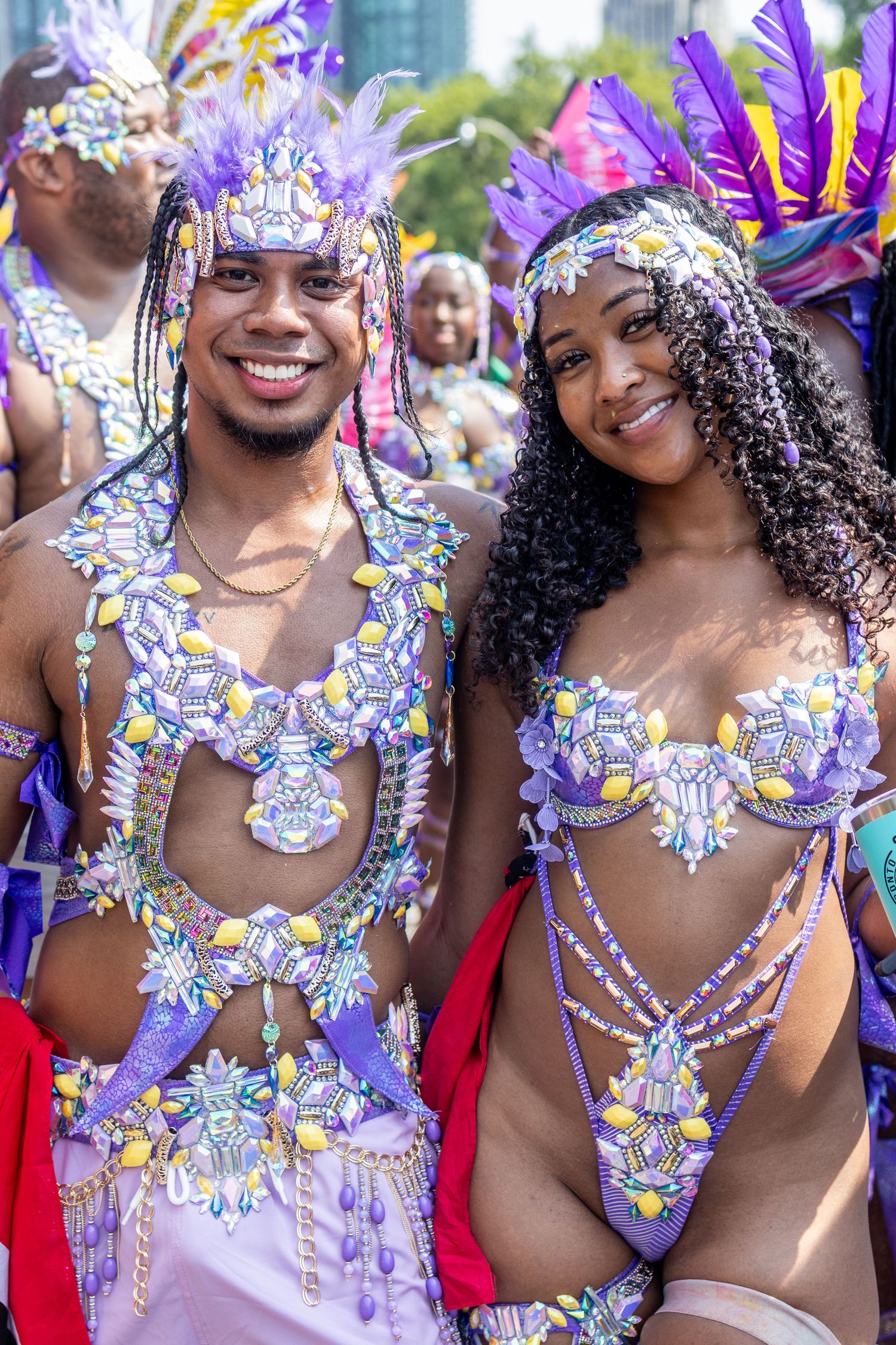Smiling couple in matching purple jeweled carnival costumes posing together at a street festival.