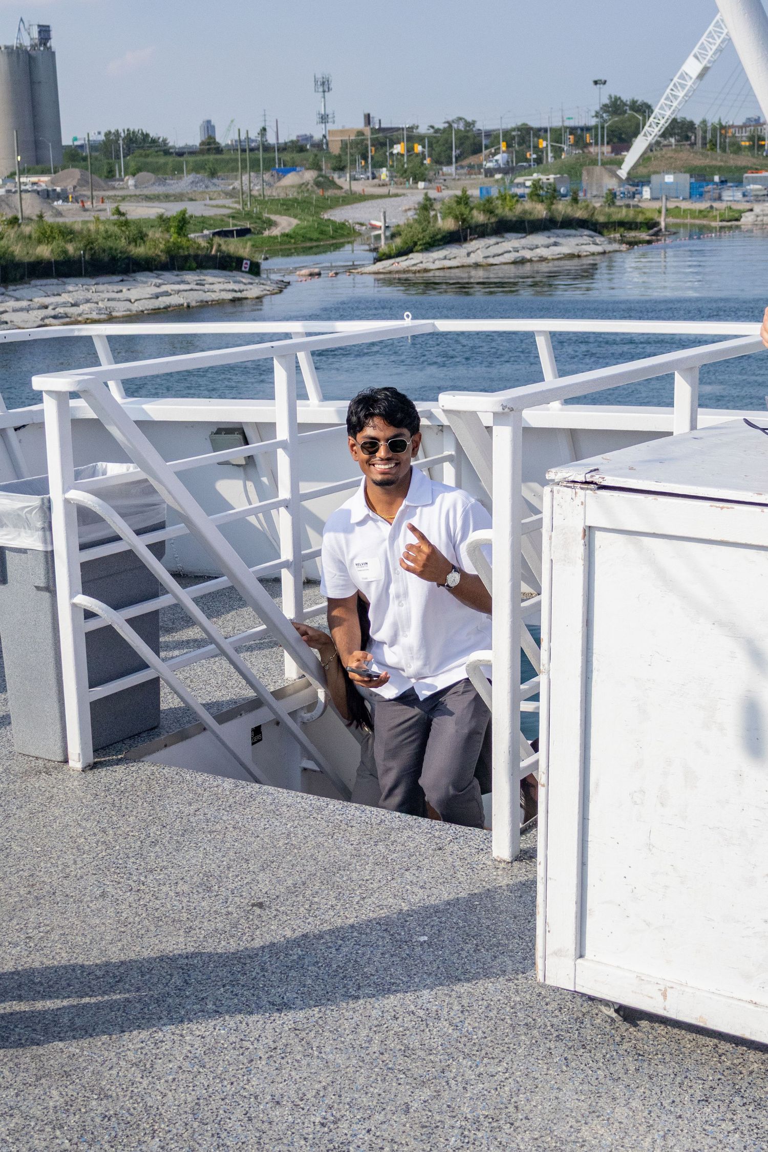 Young man in white shirt with sunglasses posing on a boat deck near waterway.