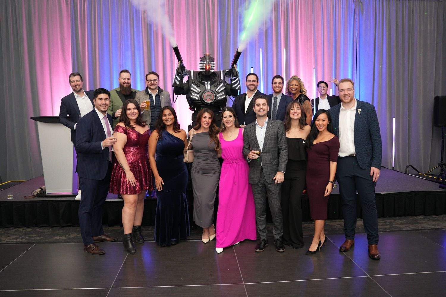 Large group of colleagues posing together at a formal gala event with a costumed mascot.