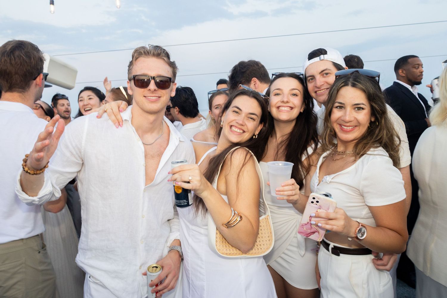Group of friends in white outfits smiling together at an outdoor evening party.