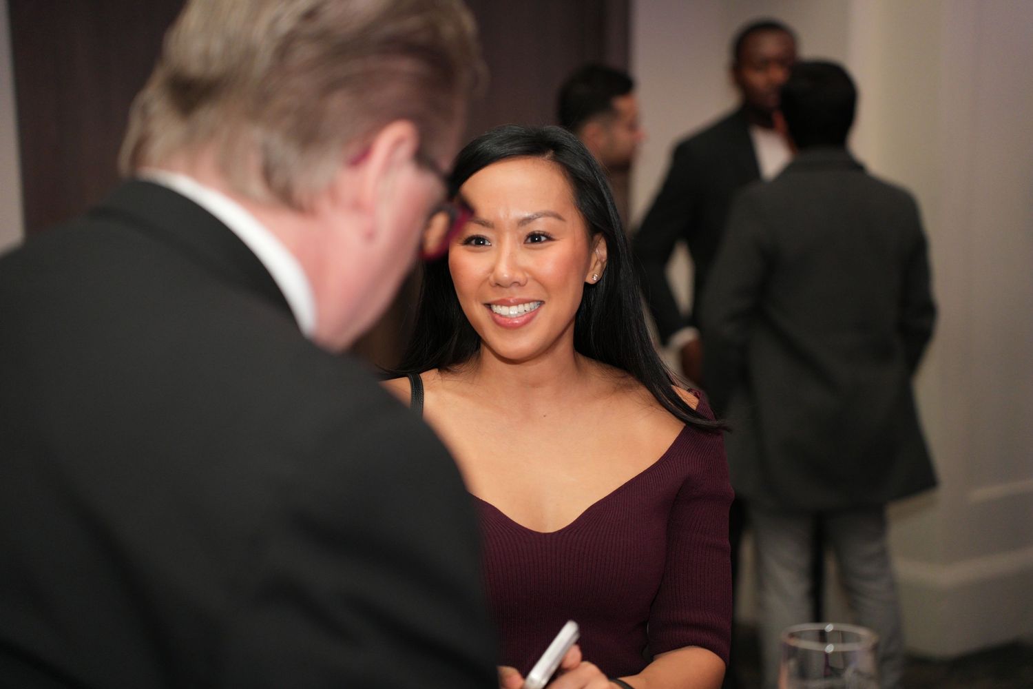 Woman in burgundy dress smiling during conversation at a professional networking event.