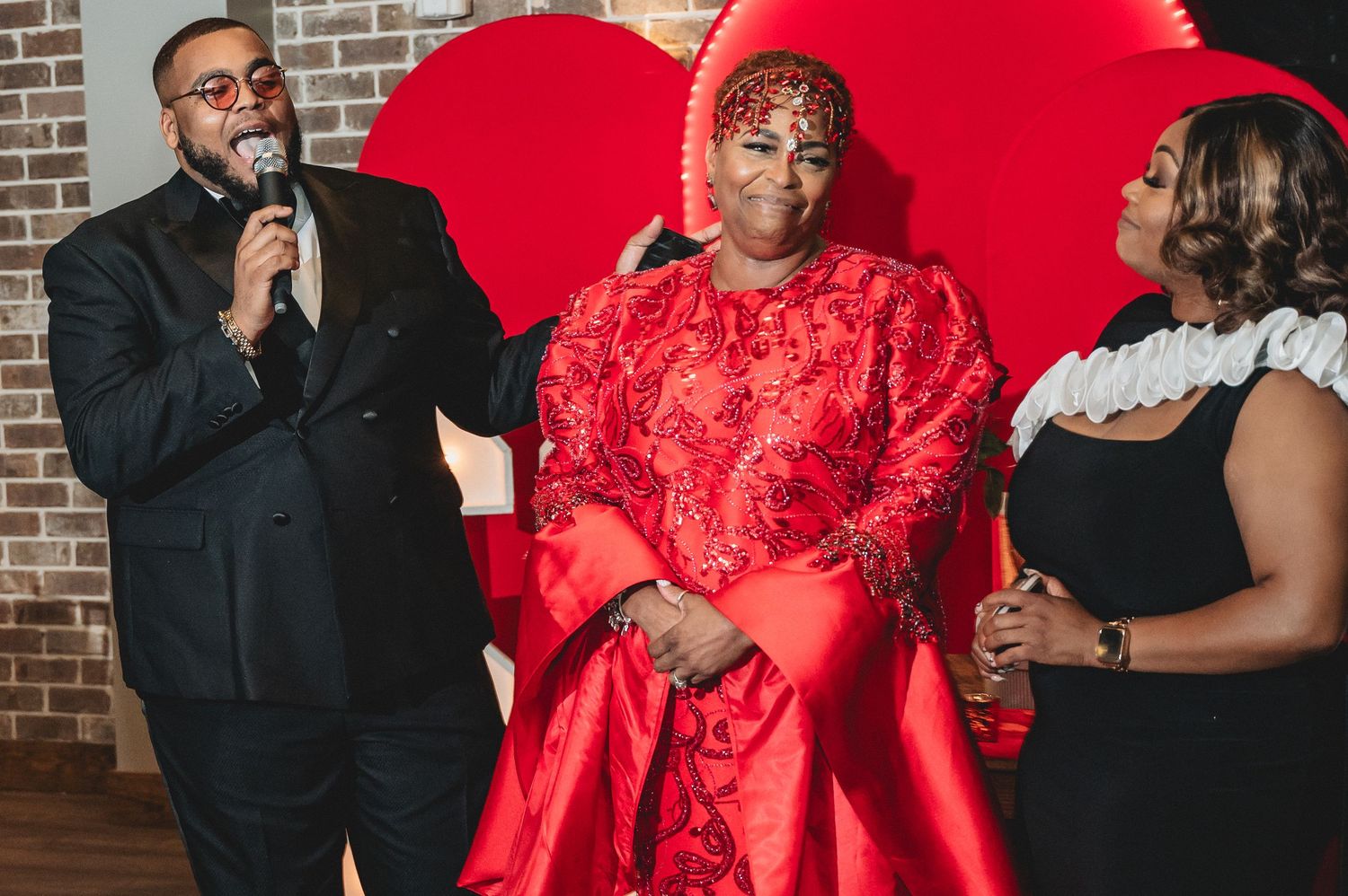 Event celebration space features bright red decor and formal attire against brick wall backdrop.