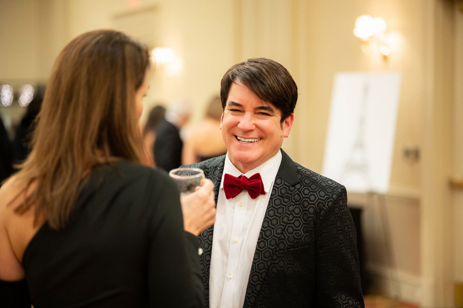 A group of formally dressed people socialize and mingle at an elegant indoor event with warm lighting.