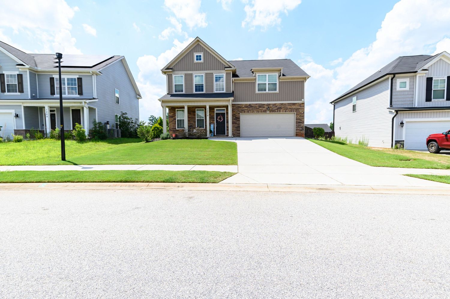 Two-story brick and siding suburban home with two-car garage, manicured lawn, and covered front porch on a quiet street.