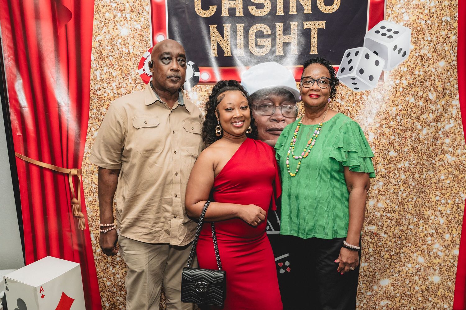 Casino party celebration with people posing against a gold sequin and red curtain backdrop.