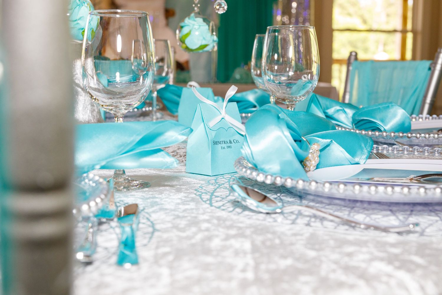 Elegant Tiffany blue wedding table setting with ribbon, pearl accents, gift boxes, and crystal glassware on white lace.