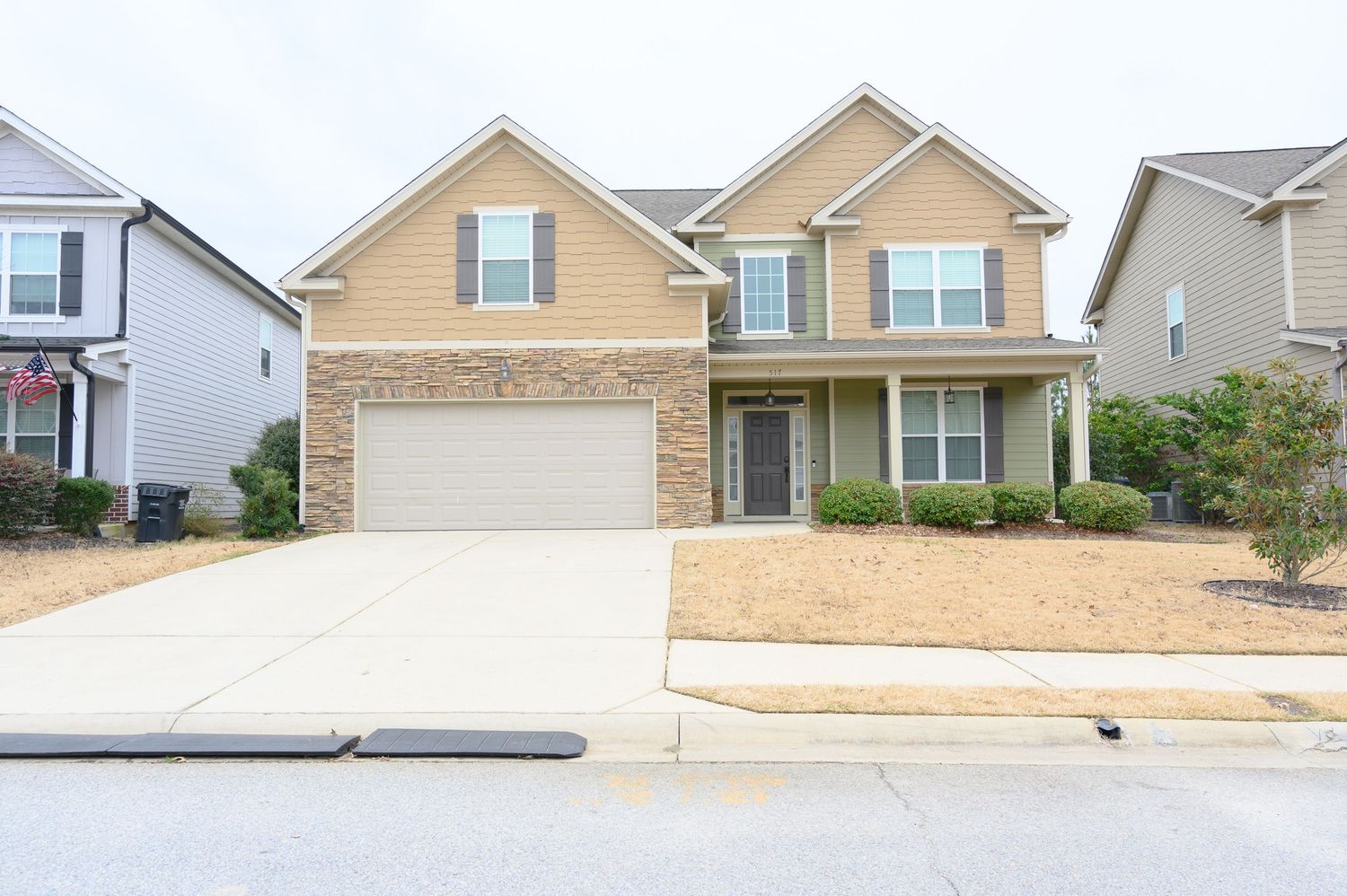 Two-story suburban home with stone and beige siding, two-car garage, and concrete driveway in a residential neighborhood.