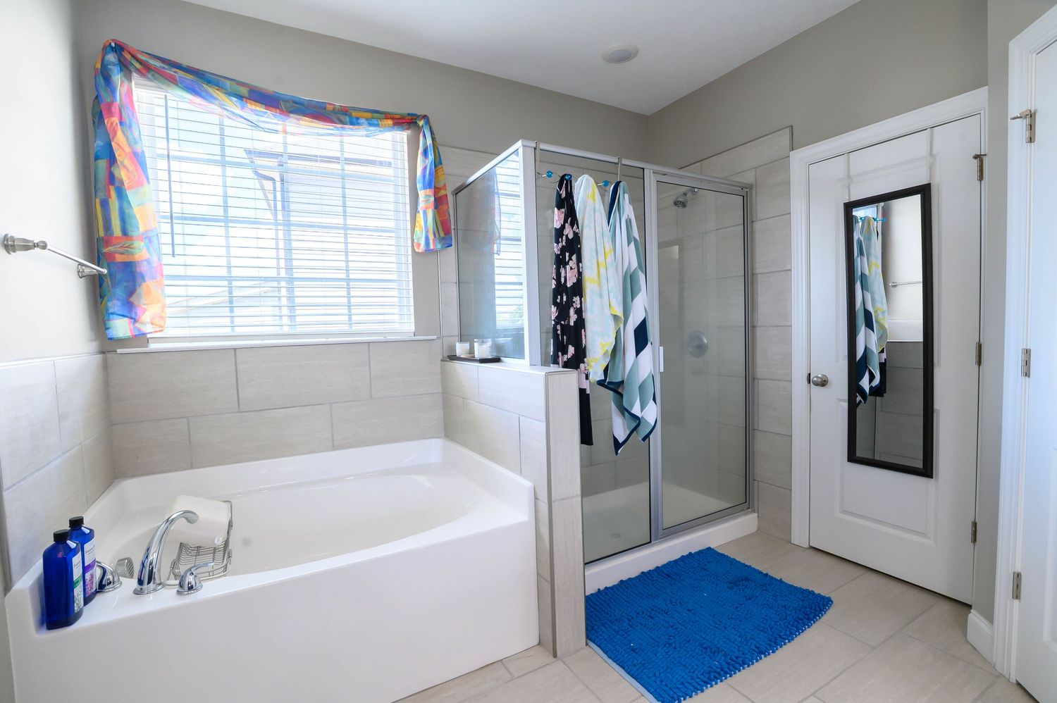 Spacious master bathroom featuring a soaking tub, glass walk-in shower, blue bath mat, and white tile flooring.