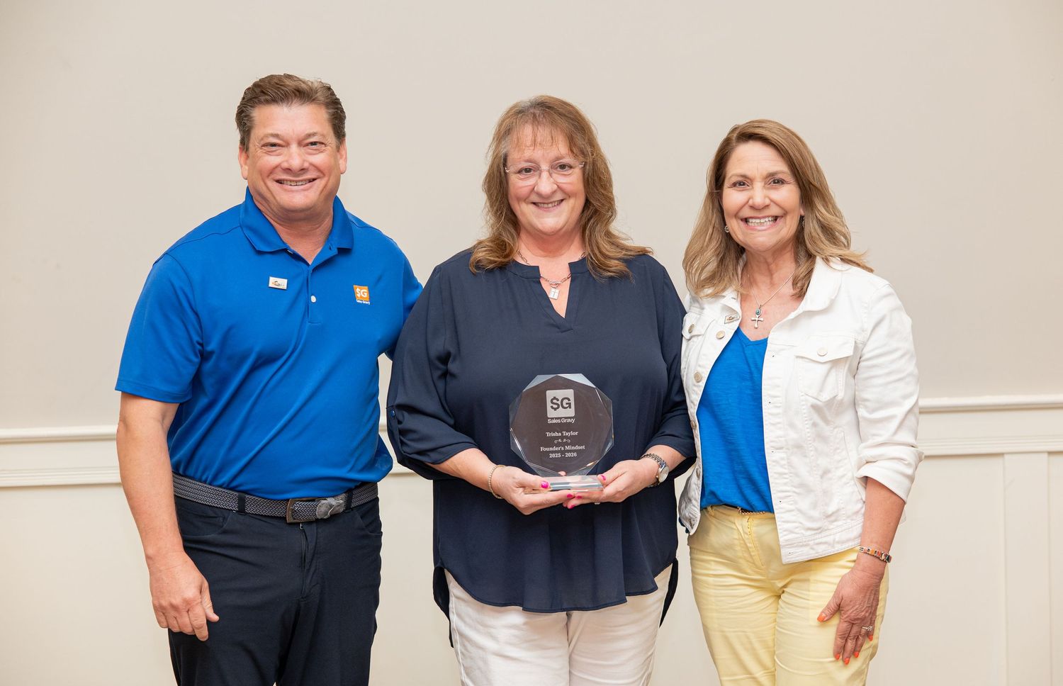 Three professionals pose together at an awards ceremony, with a woman holding a glass achievement award plaque.