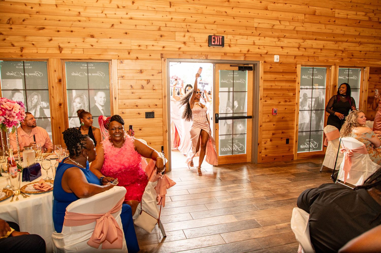 Wedding guests seated at decorated tables as a woman in white makes a grand entrance into the reception hall.