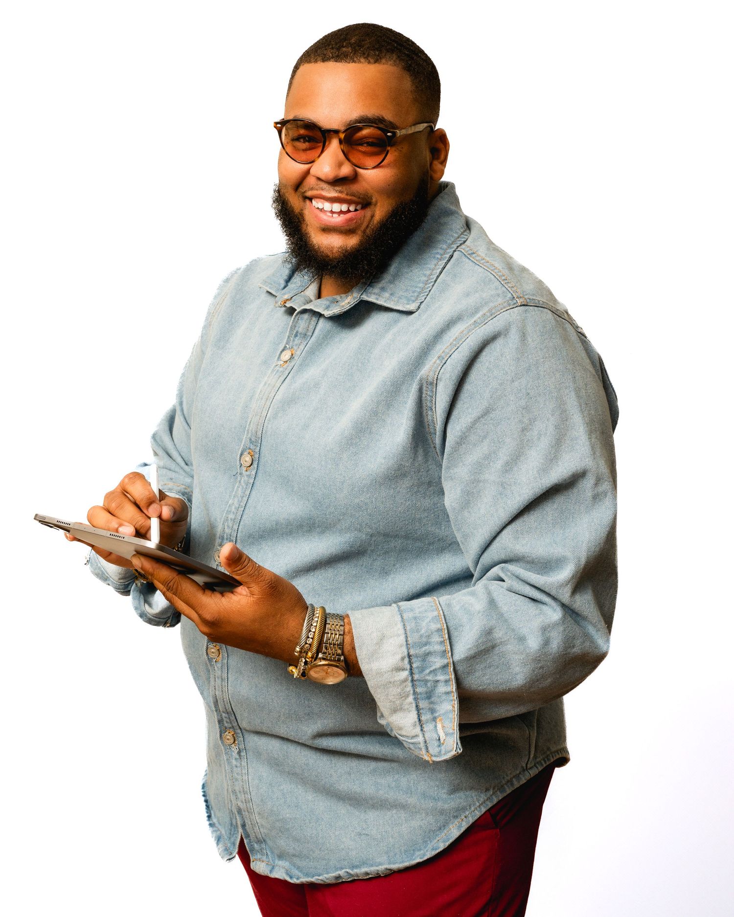 Person in light denim shirt and red pants smiling while holding a mobile device.