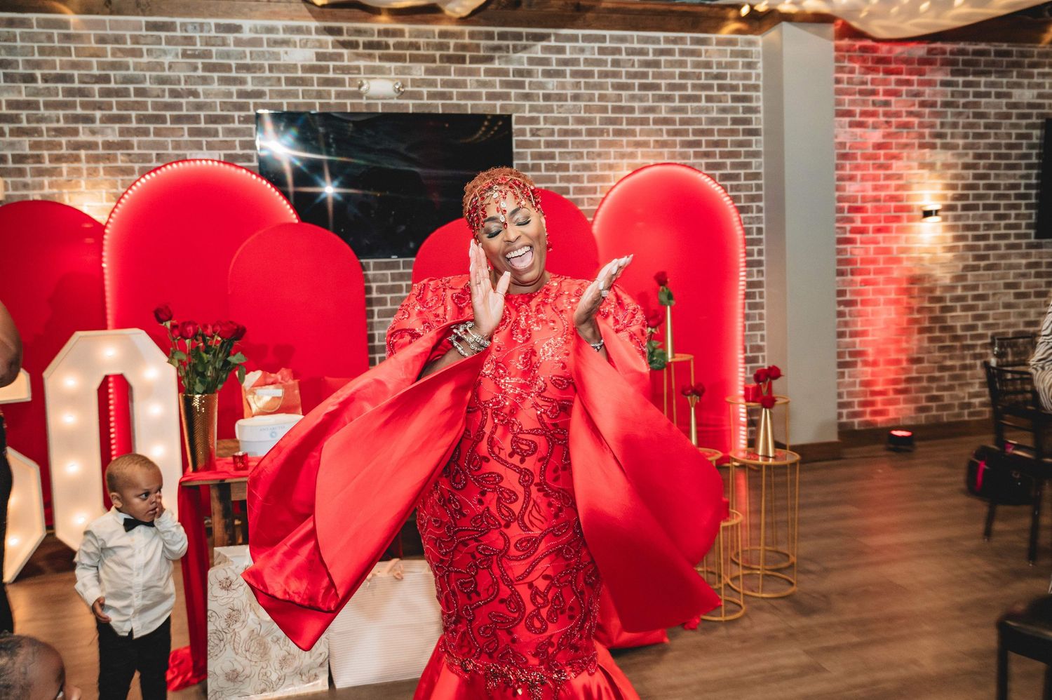 A line of large red heart-shaped balloons decorates a rustic brick wall venue with ambient lighting in the background.
