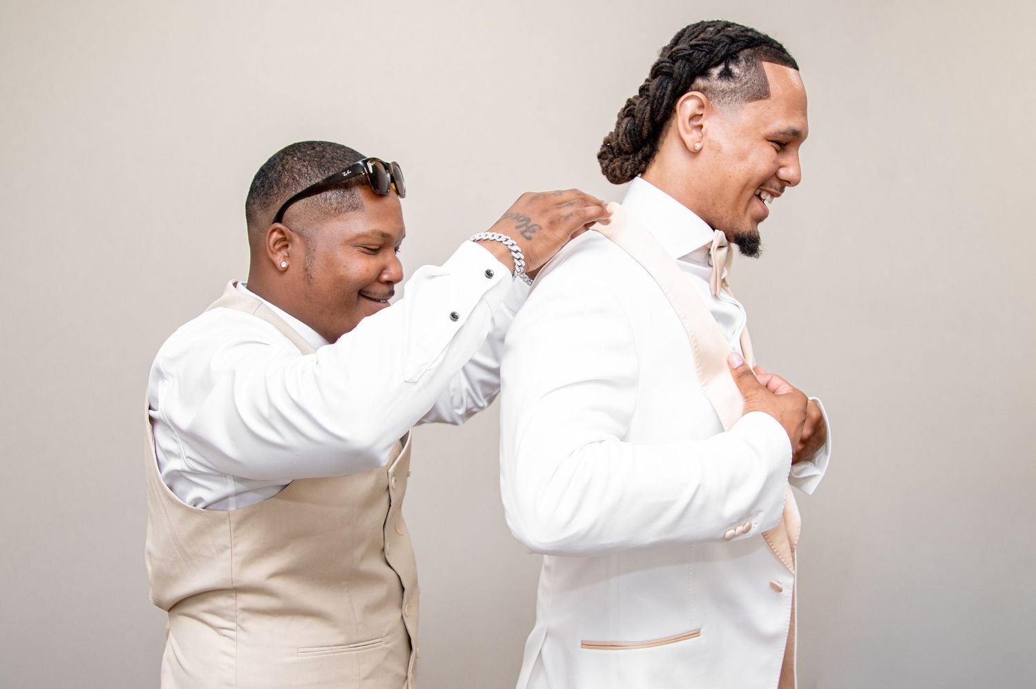 Two men in wedding attire, one adjusting the other's white tuxedo jacket collar.
