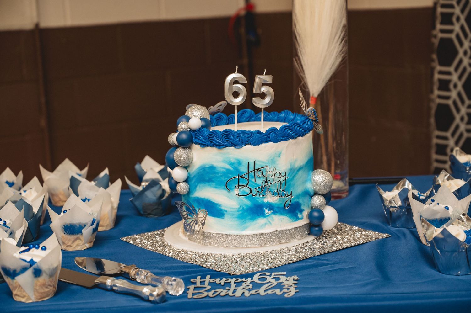 Elegant blue and silver themed cake display with crowns and decorative elements on a white tablecloth.