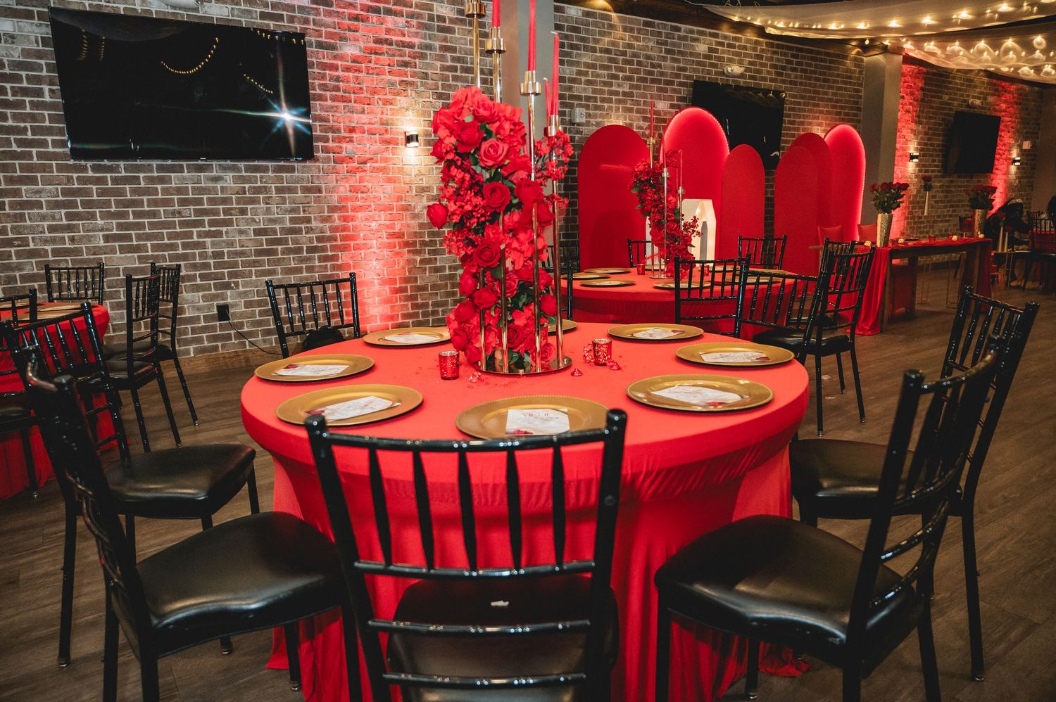 An elegant wedding reception venue with red tablecloths, brick walls, and ambient string lighting creates a romantic atmosphere.