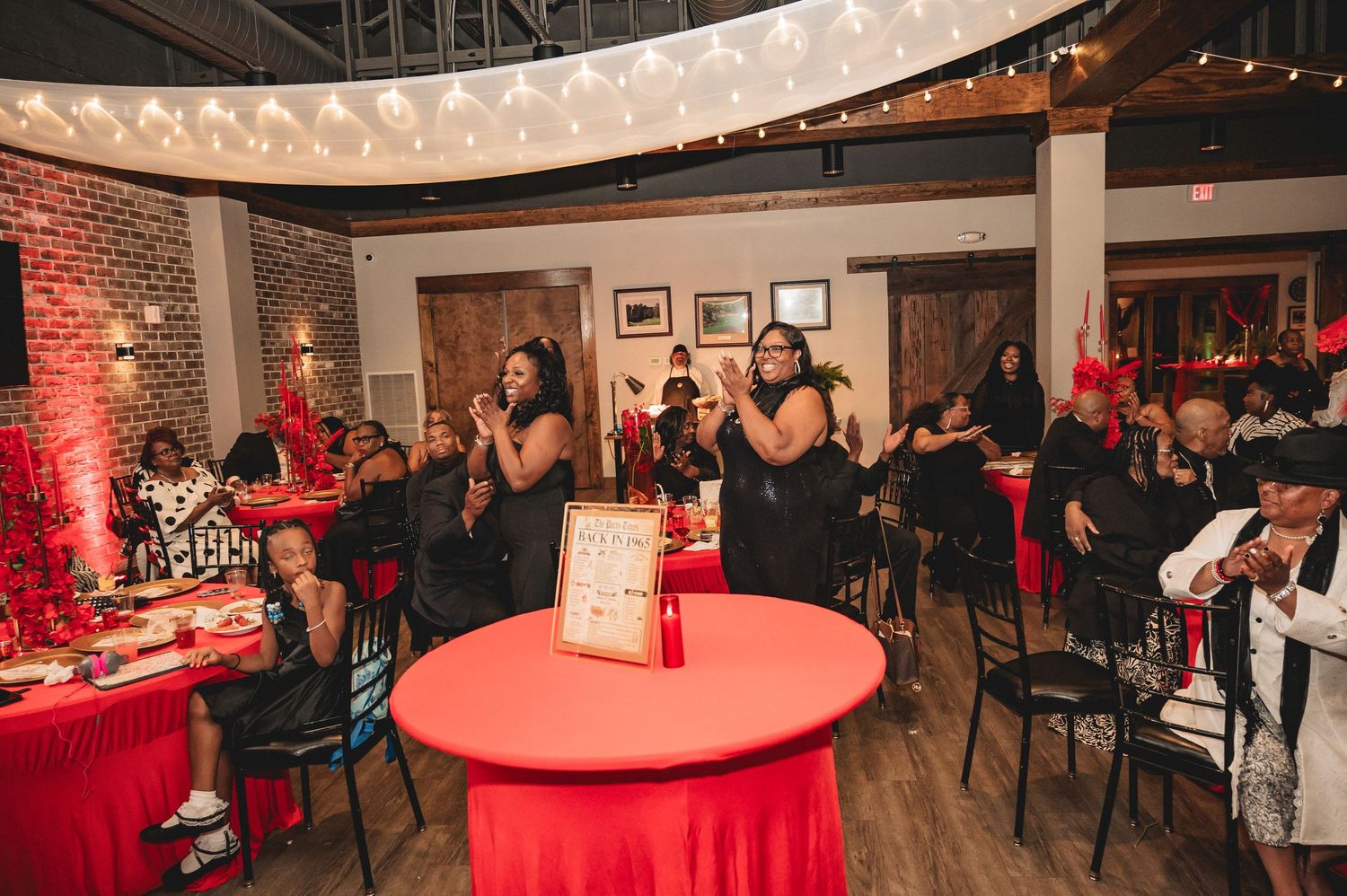 Modern event venue featuring exposed brick walls, string lights, and red accent lighting creating an intimate atmosphere.