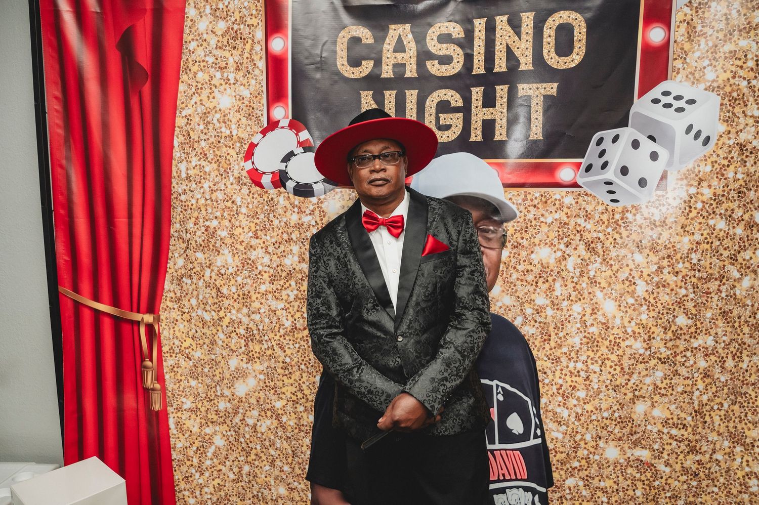 Casino night party backdrop with gold sequins, dice decorations and red curtains.
