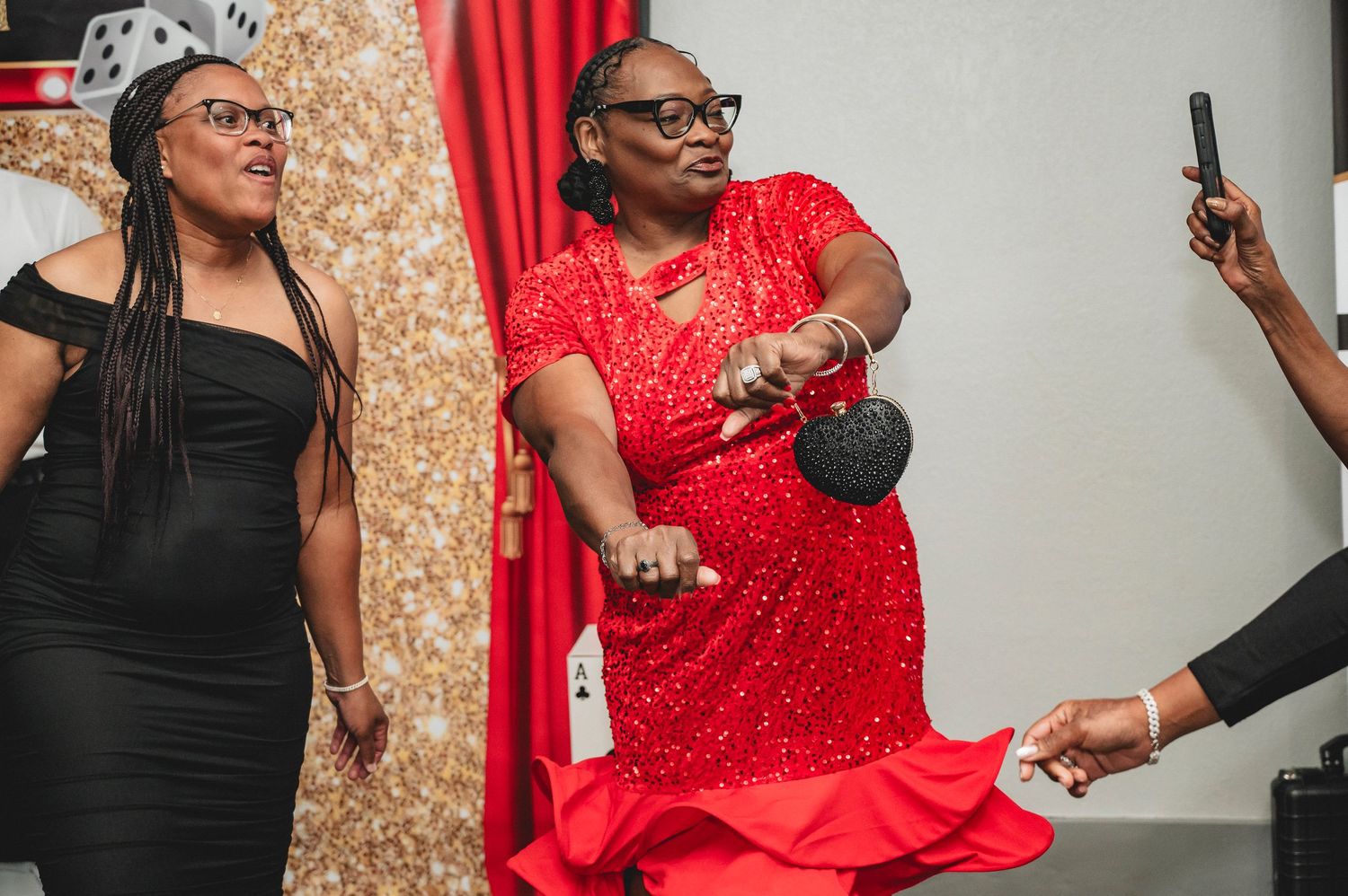 Party guests laughing and mingling in front of a glittering gold backdrop with red curtains.