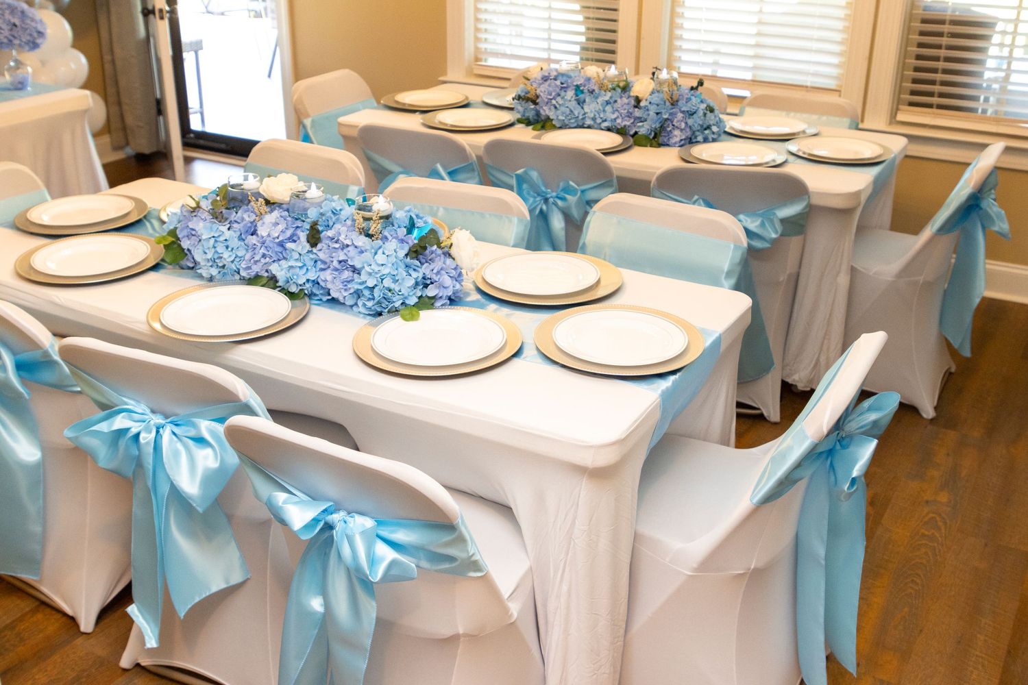 White chairs with turquoise blue sashes line both sides of long banquet tables set with white plates and blue centerpieces.