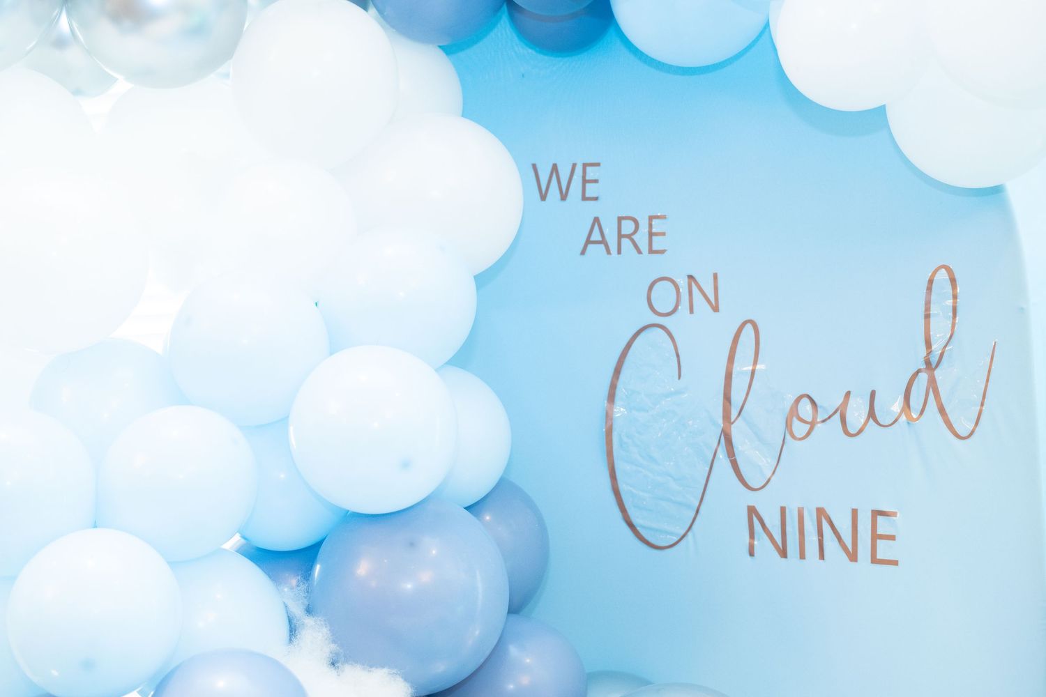 Dreamy blue balloon arch with 'We Are On Cloud Nine' text against a light blue background with white clouds.