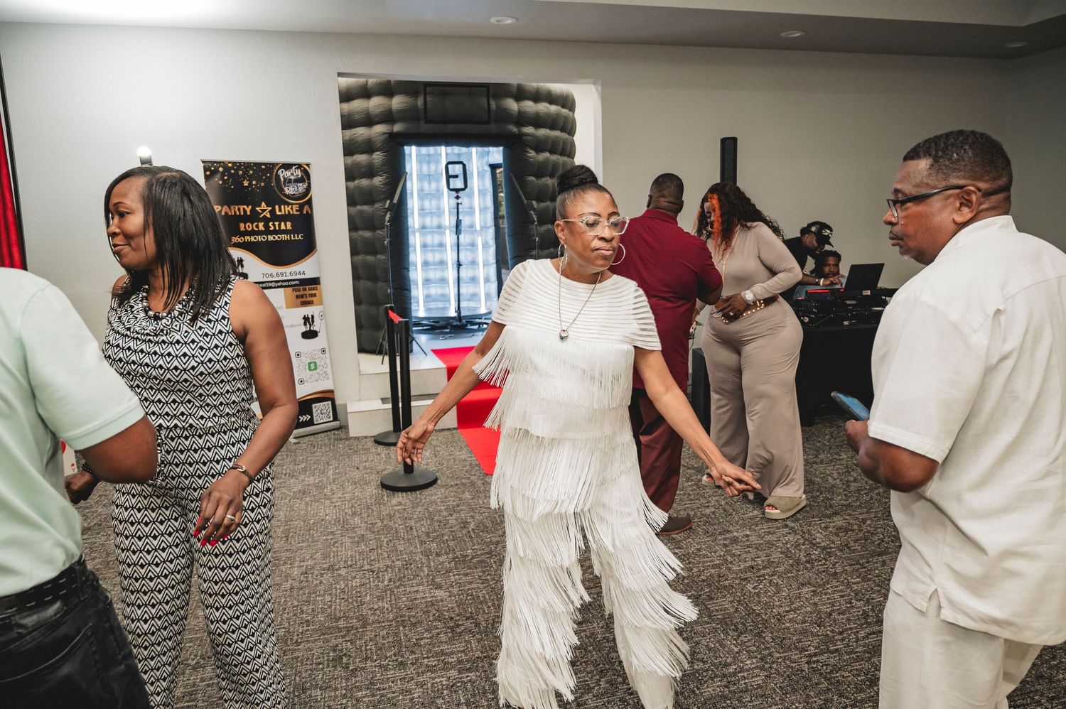 People in white and casual outfits dance together in a large indoor party space.