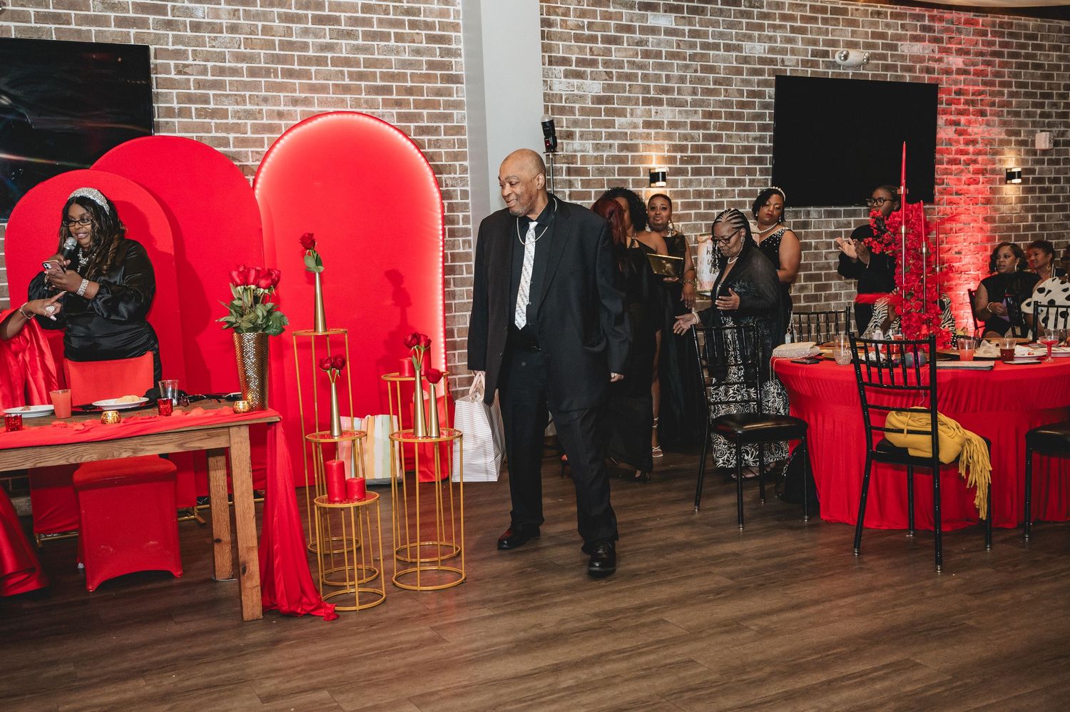 Red-themed celebration event in a brick-walled venue with guests mingling around cocktail tables.