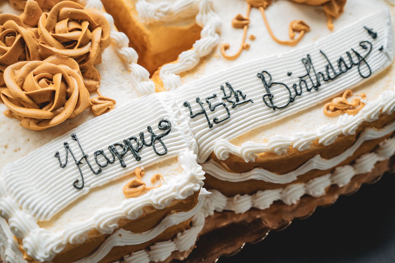 White frosted birthday cake with happy birthday text and intricate brown buttercream rose decorations.