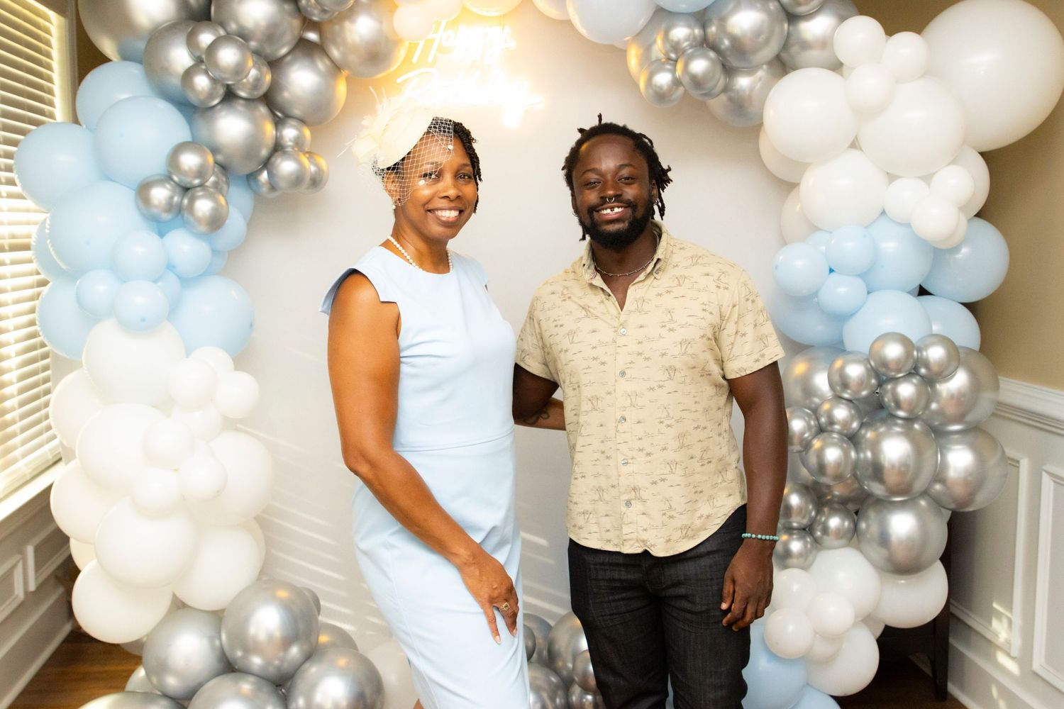 Couple posing together under an elegant arch of blue, white and silver balloons at a celebration.