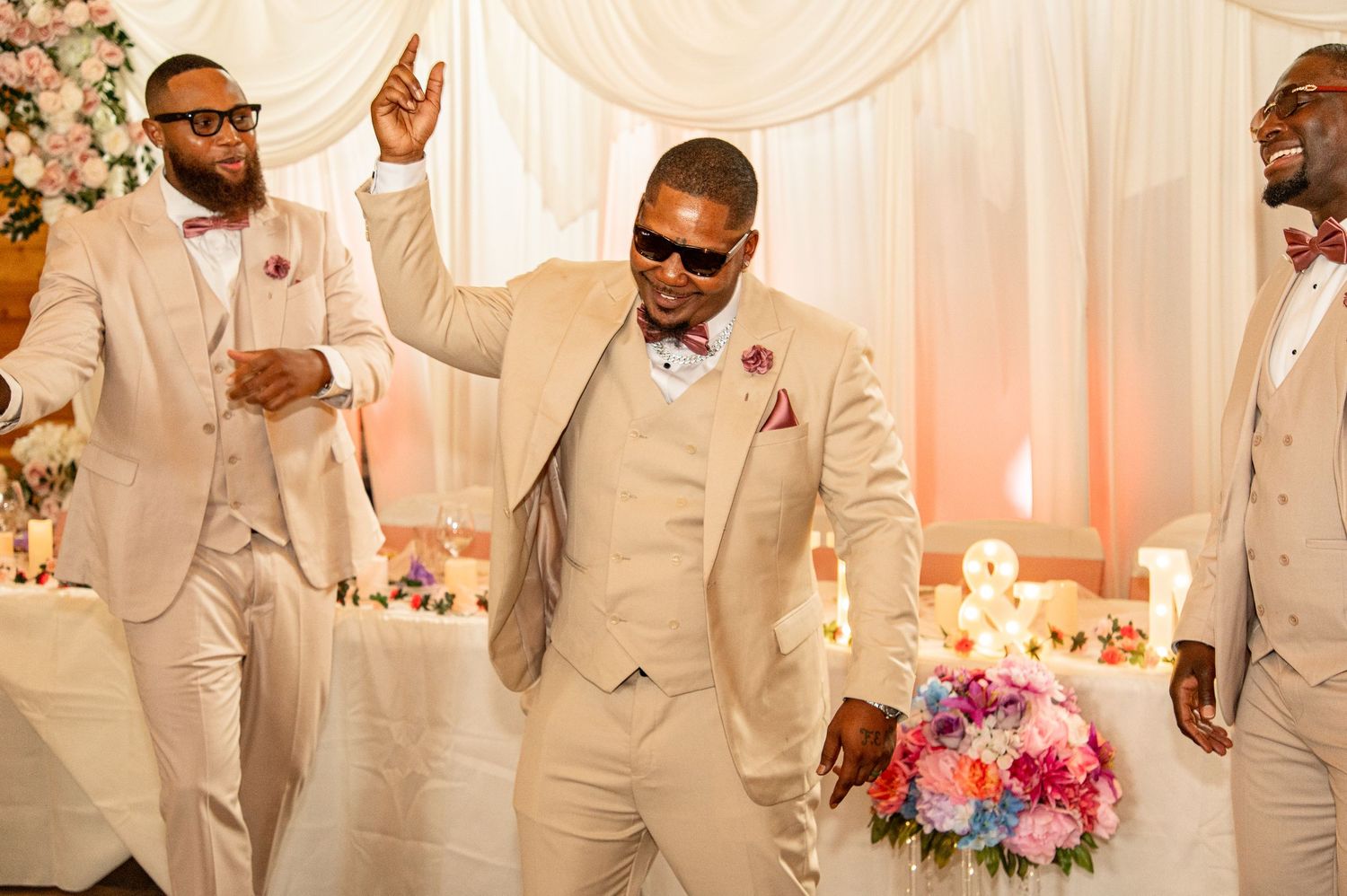 Groom dancing joyfully with groomsmen in beige suits at wedding reception.