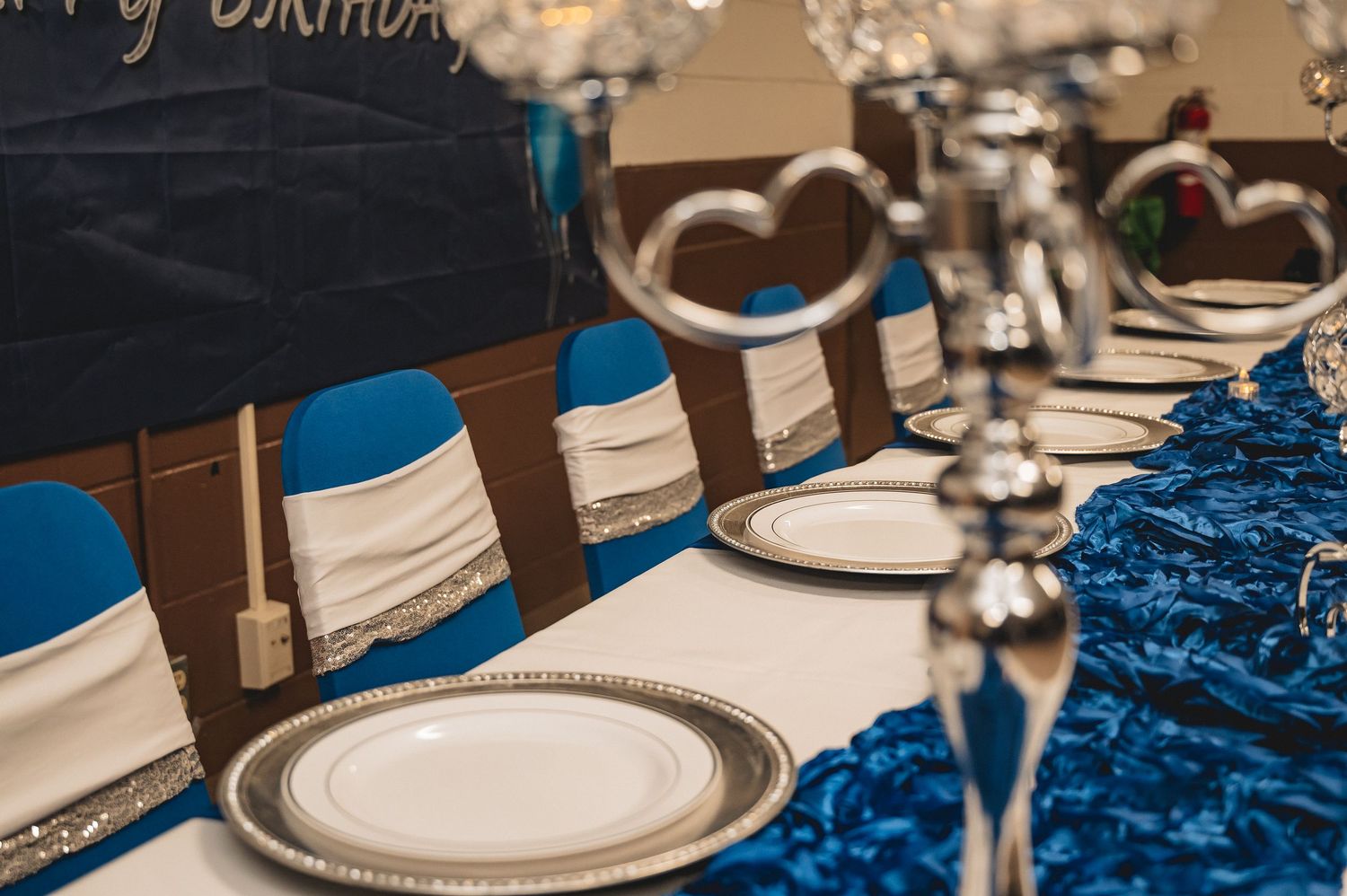 Birthday party dessert table decorated in white and royal blue with plates and crowns as party favors.
