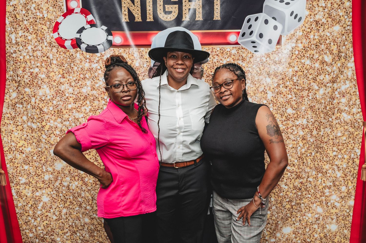 Casino night party photo with guests posing against a gold sparkle backdrop with dice decorations.
