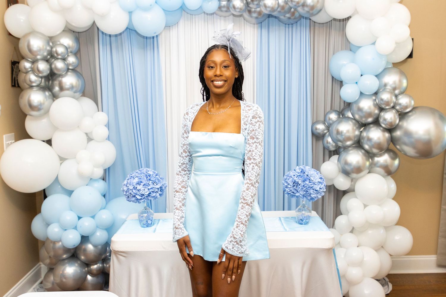 A blue and white party setup with an elegant balloon arch featuring white, silver and light blue balloons against a backdrop.