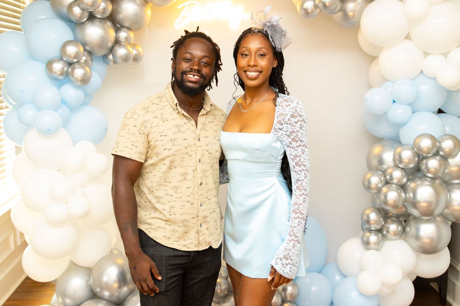 Party scene with guests in coordinated light blue and cream outfits against balloon decorations.