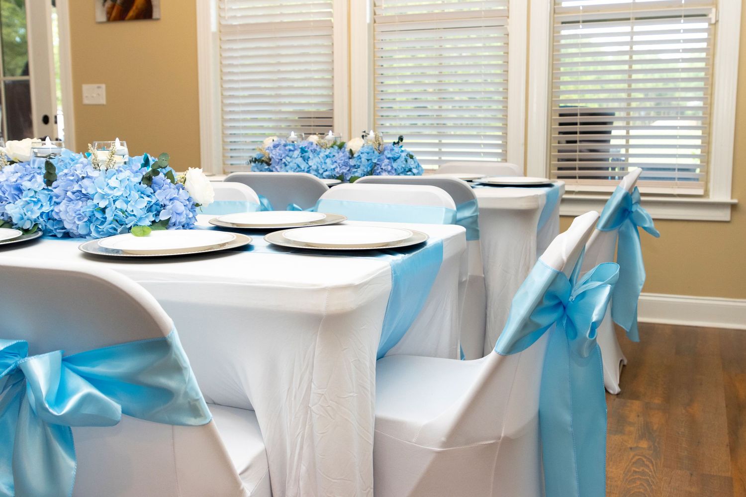 Wedding reception tables decorated with white linens and bright turquoise bows in an elegant indoor setting.