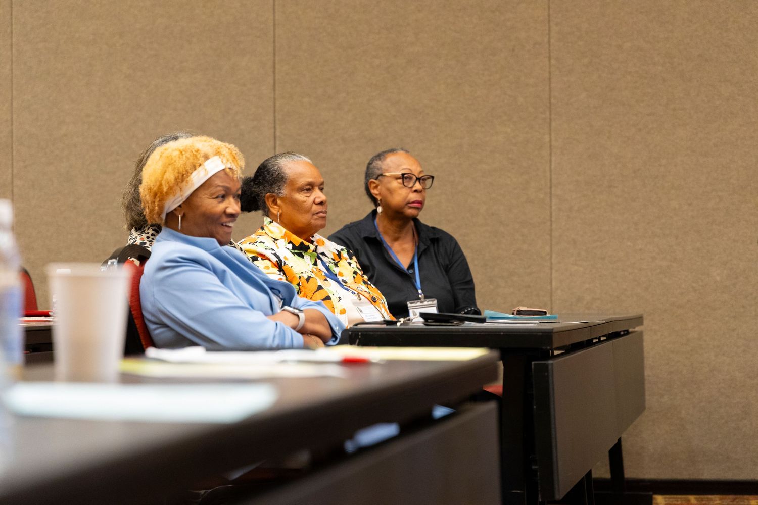 People sitting in conference room chairs during a business meeting while taking notes and participating in discussions.