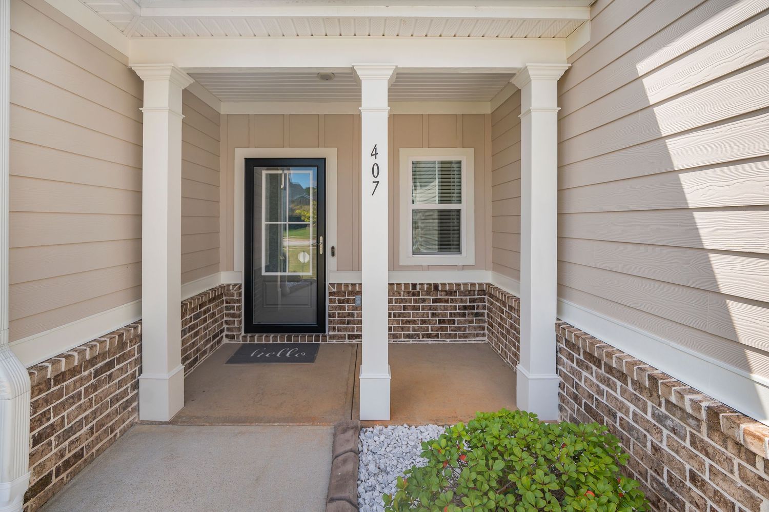 Charming home entrance with white columns, brick accents, covered porch, and black front door numbered 407.